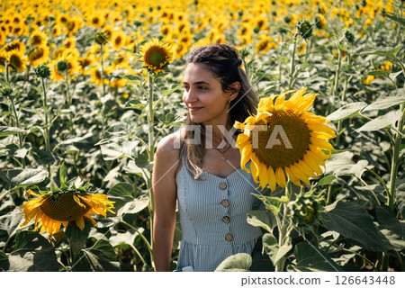 Young woman holding a sunflower on the sunflower field with blue sky. Young woman holding a sunflower on the sunflower field with blue sky. 126643448