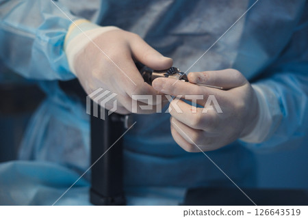 Close-up view of gloved hands meticulously preparing surgical instruments, emphasizing the precision and care essential during veterinary surgical procedures in a sterile environment. Close-up view of gloved hands meticulously preparing surgical instruments, emphasizing the precision and care essential during veterinary surgical procedures in a sterile environment. 126643519