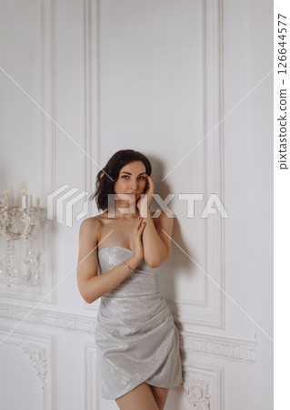 Young woman in silver dress posing against white classic wall in elegant room 126644577