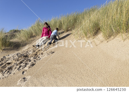 Mother and son sliding down sand dune on sunny day 126645230