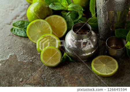 Shaker, limes, and fresh mint branches on a stone table. Shaker, limes, and fresh mint branches on a stone table. 126645594