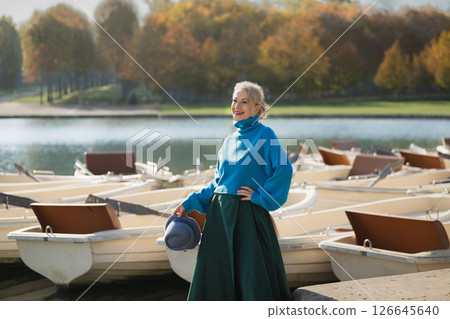 Gray-haired woman in a blue sweater against the background of boats, a lake and a forest in the Versailles park 126645640