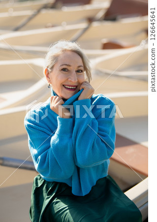 Gray-haired woman in a blue sweater against the background of boats, a lake and a forest in the Versailles park 126645641