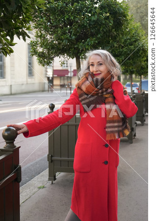 Gray-haired woman of sixty years old in a red coat and a terracotta scarf in the city Gray-haired woman of sixty years old in a red coat and a terracotta scarf in the city 126645644