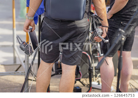 Men holding drone and tablet at an outdoor event. Drone operators preparing for an aerial shoot, showcasing modern technology in video production, event coverage Men holding drone and tablet at an outdoor event. Drone operators preparing for an aerial shoot, showcasing modern technology in video production, event coverage 126645753