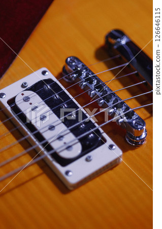 Close-up of electric guitar bridge and pickup on wooden body with strings and red strap visible Close-up of electric guitar bridge and pickup on wooden body with strings and red strap visible 126646115
