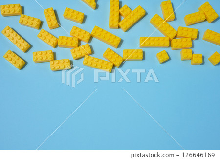 Scattered blue plastic toy building bricks on a solid yellow background. Play, construction, education or creative concept 126646169