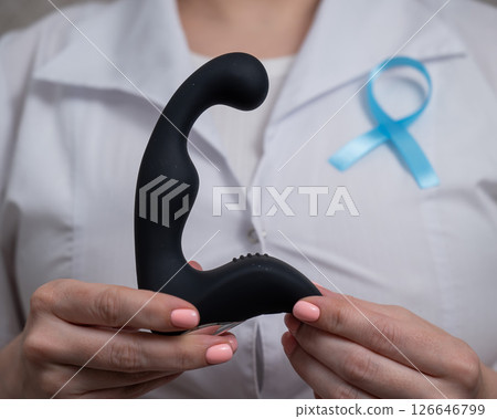 Female doctor holding prostate massager and blue ribbon. Symbol of fight against prostate cancer.  Female doctor holding prostate massager and blue ribbon. Symbol of fight against prostate cancer.  126646799