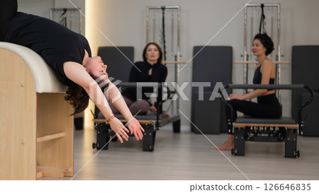 Three women doing Pilates on a reformer and a Pilates barrel.  126646835