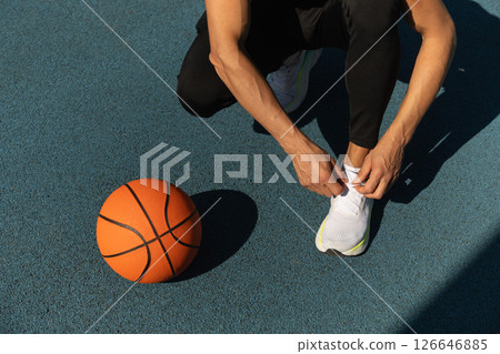 Close up basketball player tying sports shoes in basketball court outdoors. Last preparation. Team game. Close up basketball player tying sports shoes in basketball court outdoors. Last preparation. Team game. 126646885