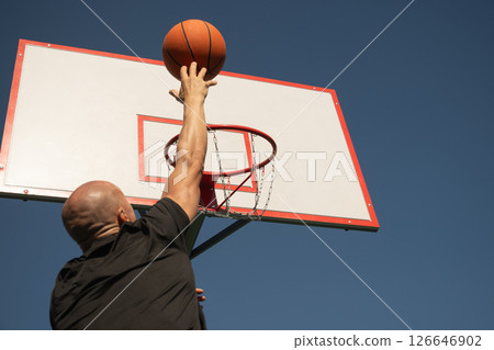 Basketball player or sporty man tries to throw ball into basketball hoop on sports court at courtyard. Street style. Game moment. Close up. Basketball player or sporty man tries to throw ball into basketball hoop on sports court at courtyard. Street style. Game moment. Close up. 126646902