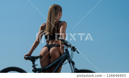 Caucasian woman with a stunning athletic figure in short shorts rides a bike against the blue sky Caucasian woman with a stunning athletic figure in short shorts rides a bike against the blue sky 126646903