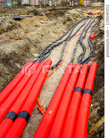 Laying new underground high-voltage power cable in red corrugated protective tube 126646952