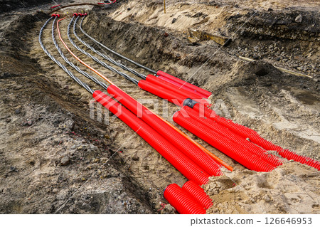 Laying new underground high-voltage power cable in red corrugated protective tube 126646953