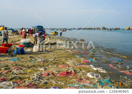 Polluted coastal fishing area with local vendors and boats along a trash-covered beach in Vietnam 126646965