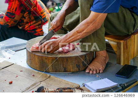 Street butcher preparing fresh pork on a wooden chopping block at a traditional open-air market 126646969