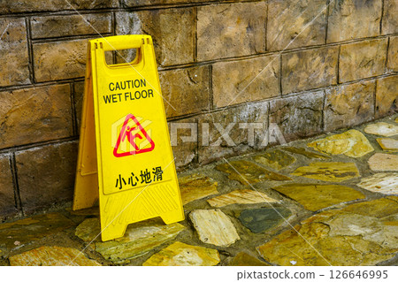 Yellow caution wet floor sign with English and Chinese text placed near a stone wall on wet surface 126646995