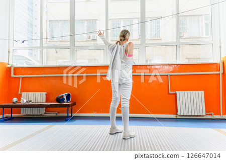 Female fencer putting on protective gear before match indoors. Female fencer putting on protective gear before match indoors. 126647014
