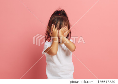 Little Asian girl covering her face with hands from fear, is afraid of something, is experiencing horror standing on a pink isolated background. Children's fears and phobias concept. 126647280