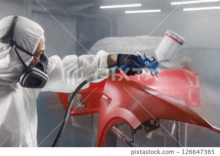 Car painter sprays red color paint to part of vehicle using spray gun in workshop garage. Complex repair and restoration automobile with exact select of color after accident. Car painter sprays red color paint to part of vehicle using spray gun in workshop garage. Complex repair and restoration automobile with exact select of color after accident. 126647365