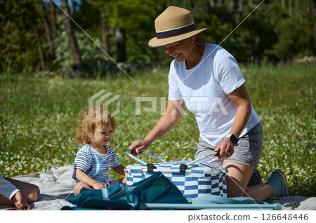 Smiling Woman and Child Enjoying a Picnic in a Scenic Outdoor Setting 126648446