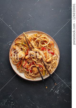 Asian udon noodles with chicken and vegetables sprinkled with sesame seeds on dark background top view Asian udon noodles with chicken and vegetables sprinkled with sesame seeds on dark background top view 126650091