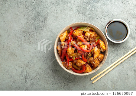Asian stir fry chicken with red and green peppers and sesame seeds in bowl with chopsticks and soy sauce top view Asian stir fry chicken with red and green peppers and sesame seeds in bowl with chopsticks and soy sauce top view 126650097