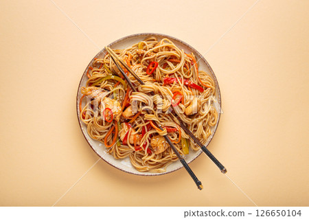 Asian chicken noodles with vegetables and chopsticks on beige background top view Asian chicken noodles with vegetables and chopsticks on beige background top view 126650104