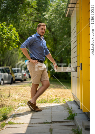 A young man is joyfully approaching a vibrant and colorful building during a sunny summer day A young man is joyfully approaching a vibrant and colorful building during a sunny summer day 126650535