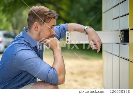 A young man interacts with a parcel locker in a pleasant outdoor setting, showcasing convenience A young man interacts with a parcel locker in a pleasant outdoor setting, showcasing convenience 126650538