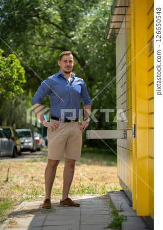 A Man Wearing a Stylish Summer Outfit Posing Outdoors Near a Bright Yellow Structure 126650548
