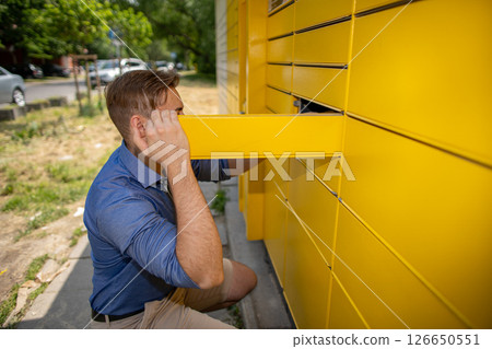 A man is utilizing a modern parcel locker system to conveniently retrieve his package effortlessly 126650551