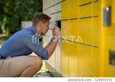 A man is utilizing a locker specifically for the purpose of retrieving a package delivery A man is utilizing a locker specifically for the purpose of retrieving a package delivery 126650552