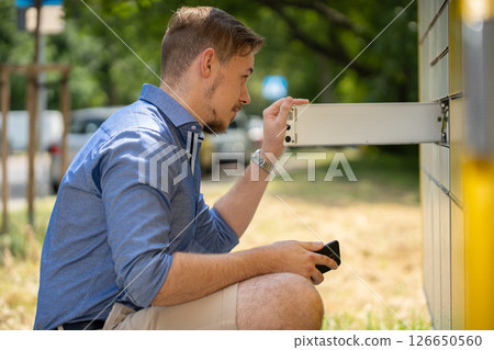 A man engaging with a smart mailbox within a serene park setting, integrating modern technology 126650560