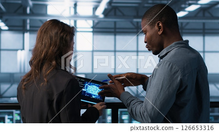 Data center system administrators using artificial intelligence neural networks tech on tablet. Teamworking server farm employees using AI programming language on device screen, camera A 126653316