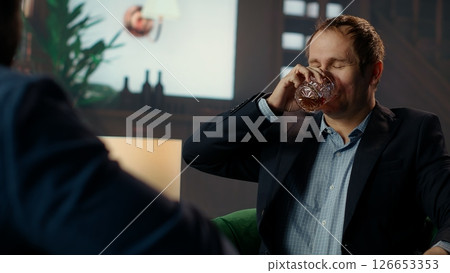 Drunk upper class elite society member being loud and obnoxious at the social club, embarrassing himself due to alcohol intoxication. Gentlemen in a state of euphoria after whiskey drinks. Camera B. 126653353