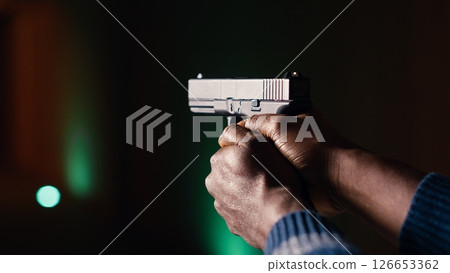 Shooting range client shoots with pistol, engaging targets at extended range. African american man at shooting ground firing lethal fire weapon, wearing protection equipment, camera B close up 126653362