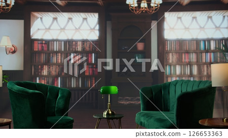 Empty cozy therapy office featuring elegant green velvet chairs, warm lighting and wooden bookshelves. Space used for counseling, psychotherapy sessions or a calming mental health space. 126653363