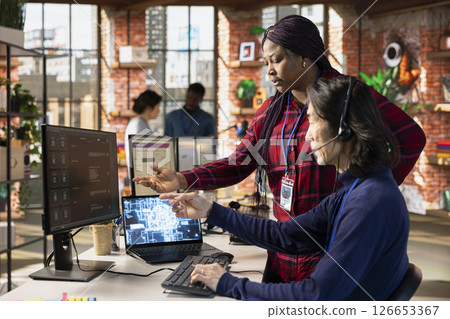 Call center supervisor guiding intern on how to use AI chatbot app on computer. African american customer support workplace onboarding specialist teaching man to use artificial intelligence software 126653367