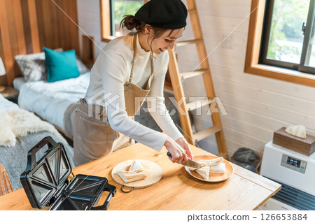 一位繫著圍裙的亞洲年輕女子正在用熱三明治機製作熱三明治 126653884