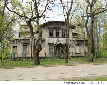 An old, abandoned Victorianstyle house is surrounded vividly by tall, lush trees nearby An old, abandoned Victorianstyle house is surrounded vividly by tall, lush trees nearby 126654152