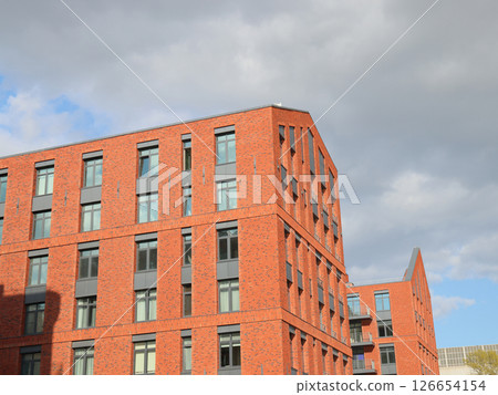 A Modern Brick Apartment Building Stands Tall Against a Dramatic Cloudy Sky Above A Modern Brick Apartment Building Stands Tall Against a Dramatic Cloudy Sky Above 126654154