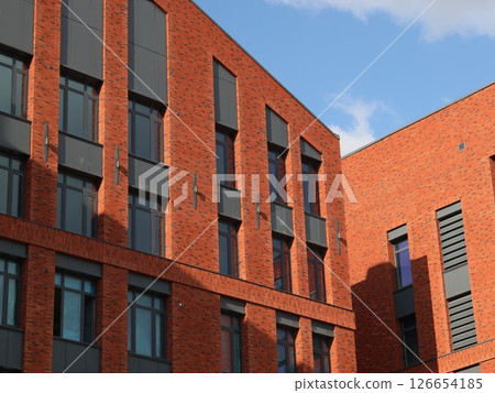 A modern brick building featuring large windows, set against a backdrop of clear skies A modern brick building featuring large windows, set against a backdrop of clear skies 126654185