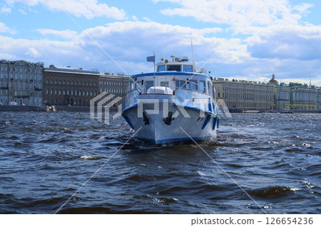 A boat gliding across tranquil water with historic buildings majestically in the background A boat gliding across tranquil water with historic buildings majestically in the background 126654236