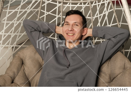 A man is sitting comfortably in a modern chair, exuding joy and radiating a cool, relaxed attitude 126654445