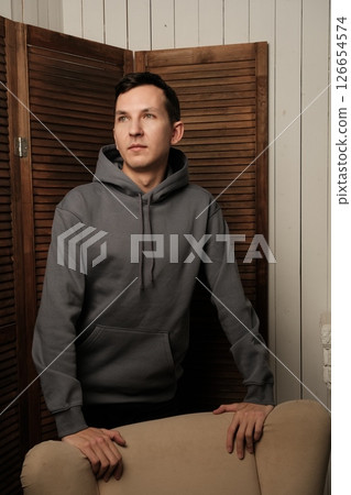 A Young Man in a Stylish Hoodie is Posing Thoughtfully Against a Contemporary Interior Backdrop A Young Man in a Stylish Hoodie is Posing Thoughtfully Against a Contemporary Interior Backdrop 126654574