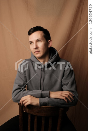 A Reflective Young Man, Dressed in Casual Attire, is Sitting Comfortably and Relaxed on a Chair A Reflective Young Man, Dressed in Casual Attire, is Sitting Comfortably and Relaxed on a Chair 126654739