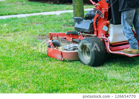 Lawn maintenance process is underway as grass trimming equipment cleans up neat yard in suburban neighborhood. Lawn maintenance process is underway as grass trimming equipment cleans up neat yard in suburban neighborhood. 126654770