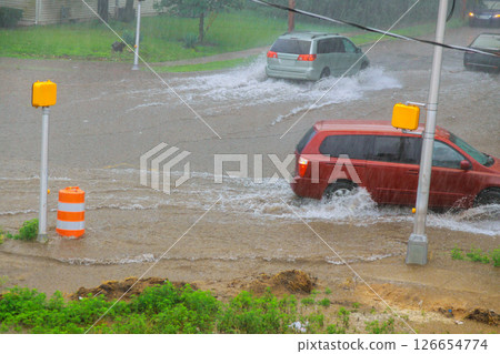 Cars drive through flooded city streets during intense rainfall, showcasing impact of severe weather on urban areas. Cars drive through flooded city streets during intense rainfall, showcasing impact of severe weather on urban areas. 126654774