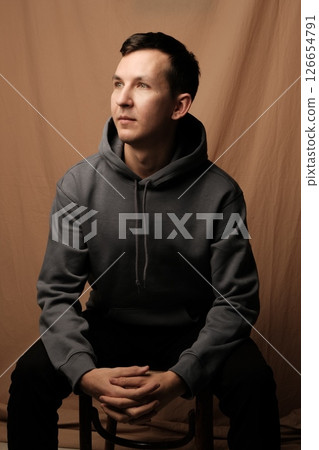 A Thoughtful and Contemplative Young Man Wearing a Casual Hoodie in a Studio Setting 126654791